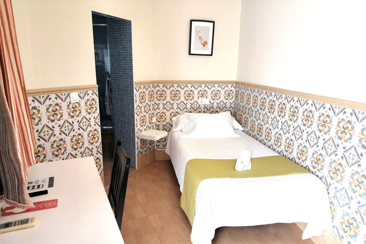 A small, neatly arranged bedroom with a bed, bedside table, and a small window.