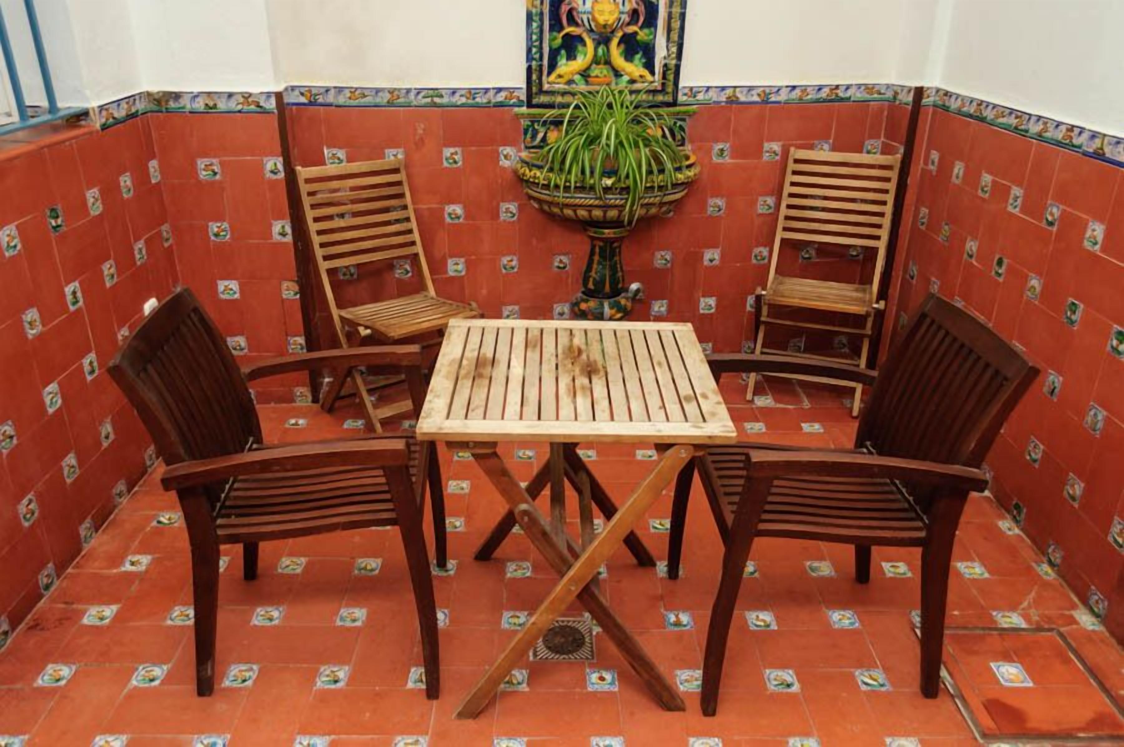 A small patio area with a wooden table and four chairs, surrounded by red-tiled walls with a decorative border.
