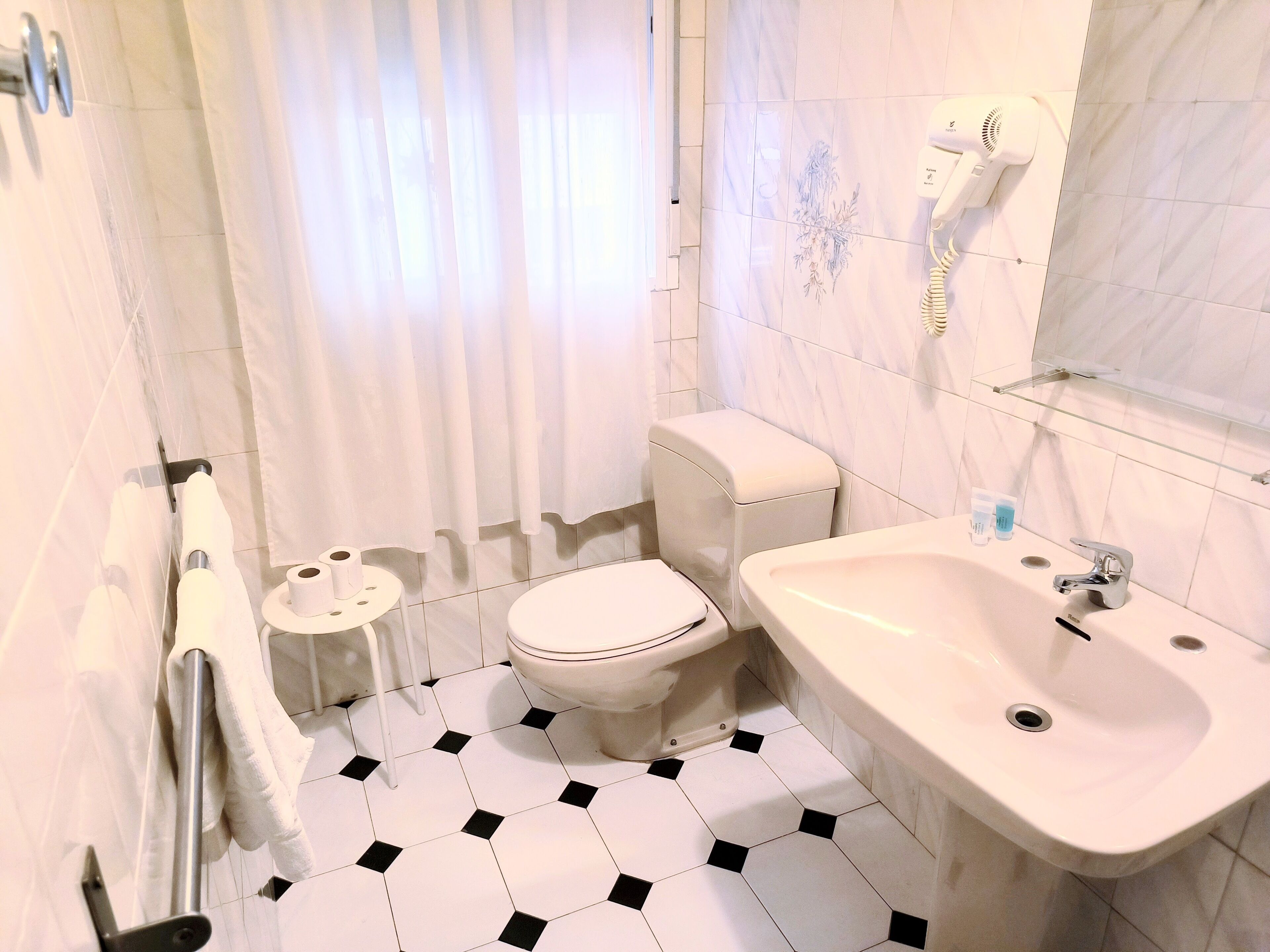 A bathroom with a toilet, bidet, sink, and a hairdryer mounted on the wall.