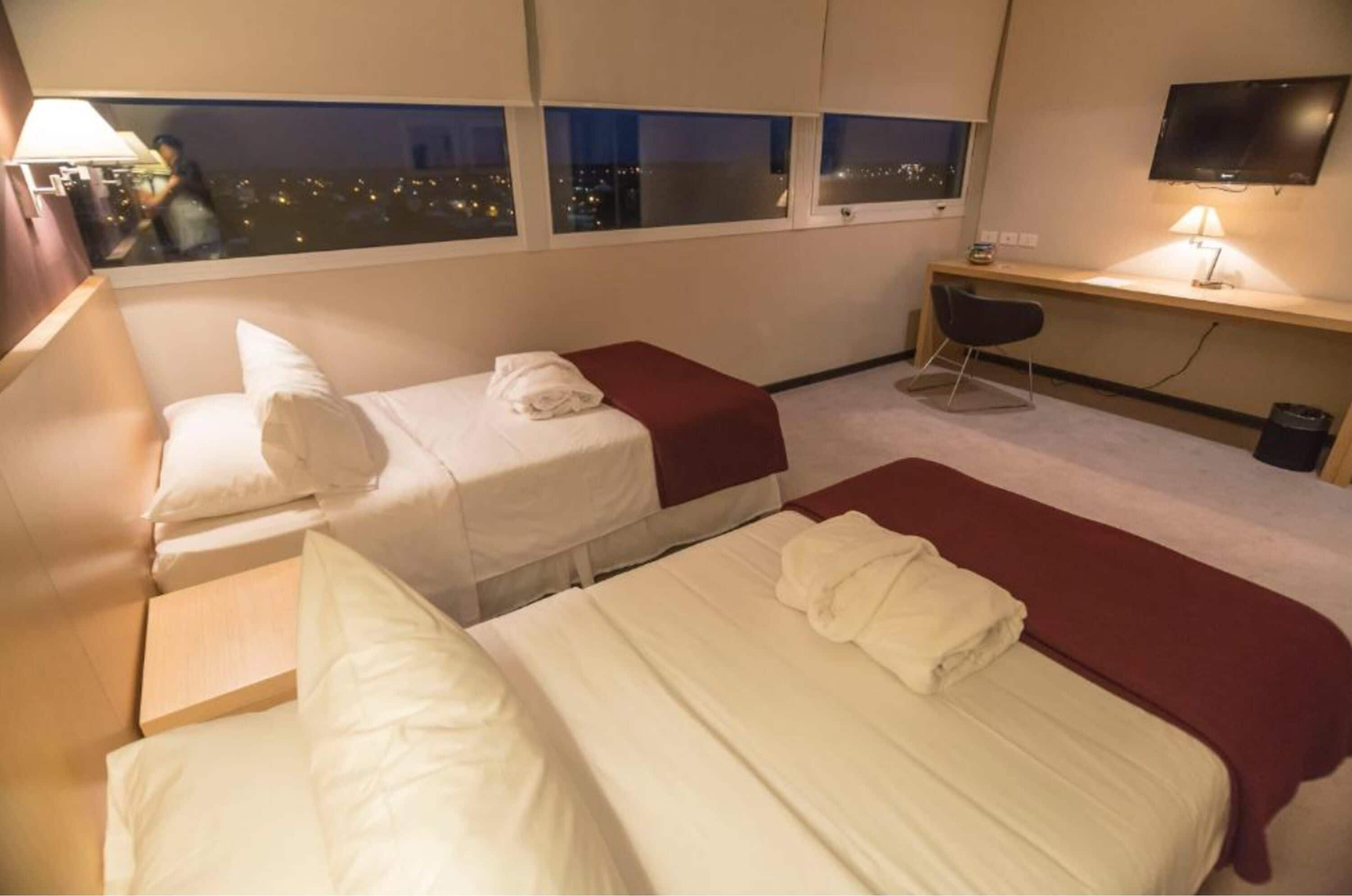 Habitación de hotel con dos camas, un escritorio, una silla y un televisor.