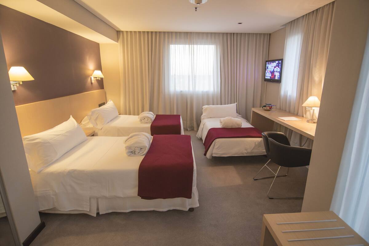 A hotel room with two beds, a desk, a chair, and a TV.