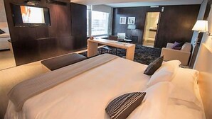 A hotel room with a large bed, a desk, a chair, a TV, and a door leading to a balcony.