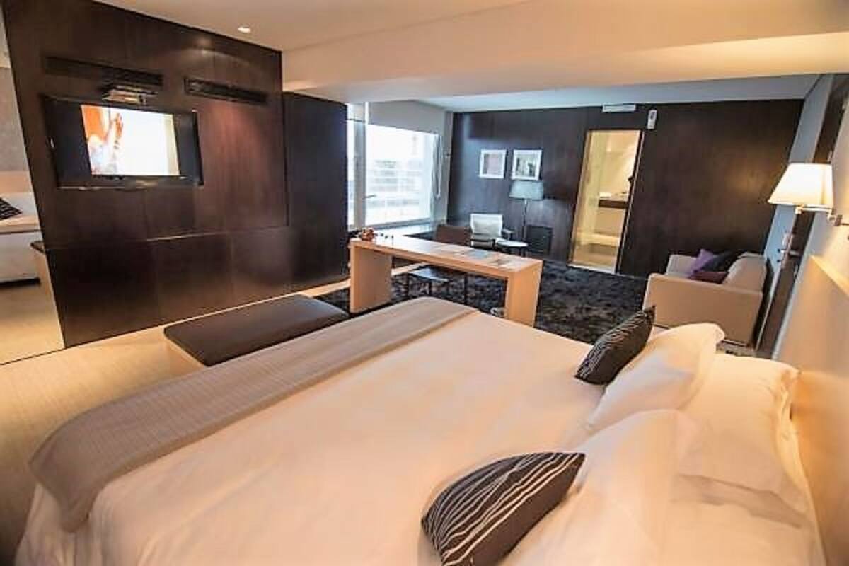 A hotel room with a large bed, a desk, a chair, a TV, and a door leading to a balcony.