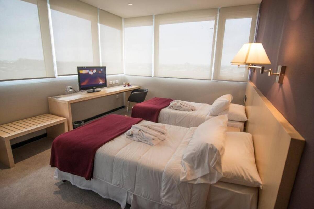 A hotel room with two beds, a desk with a computer, a chair, and a window with a view.