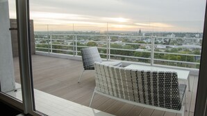 A balcony with two chairs and a table, overlooking a cityscape with buildings and trees.