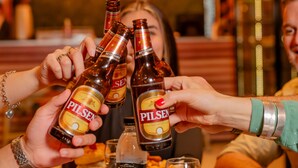 A group of people toasting with Pilsner beer bottles at a restaurant.