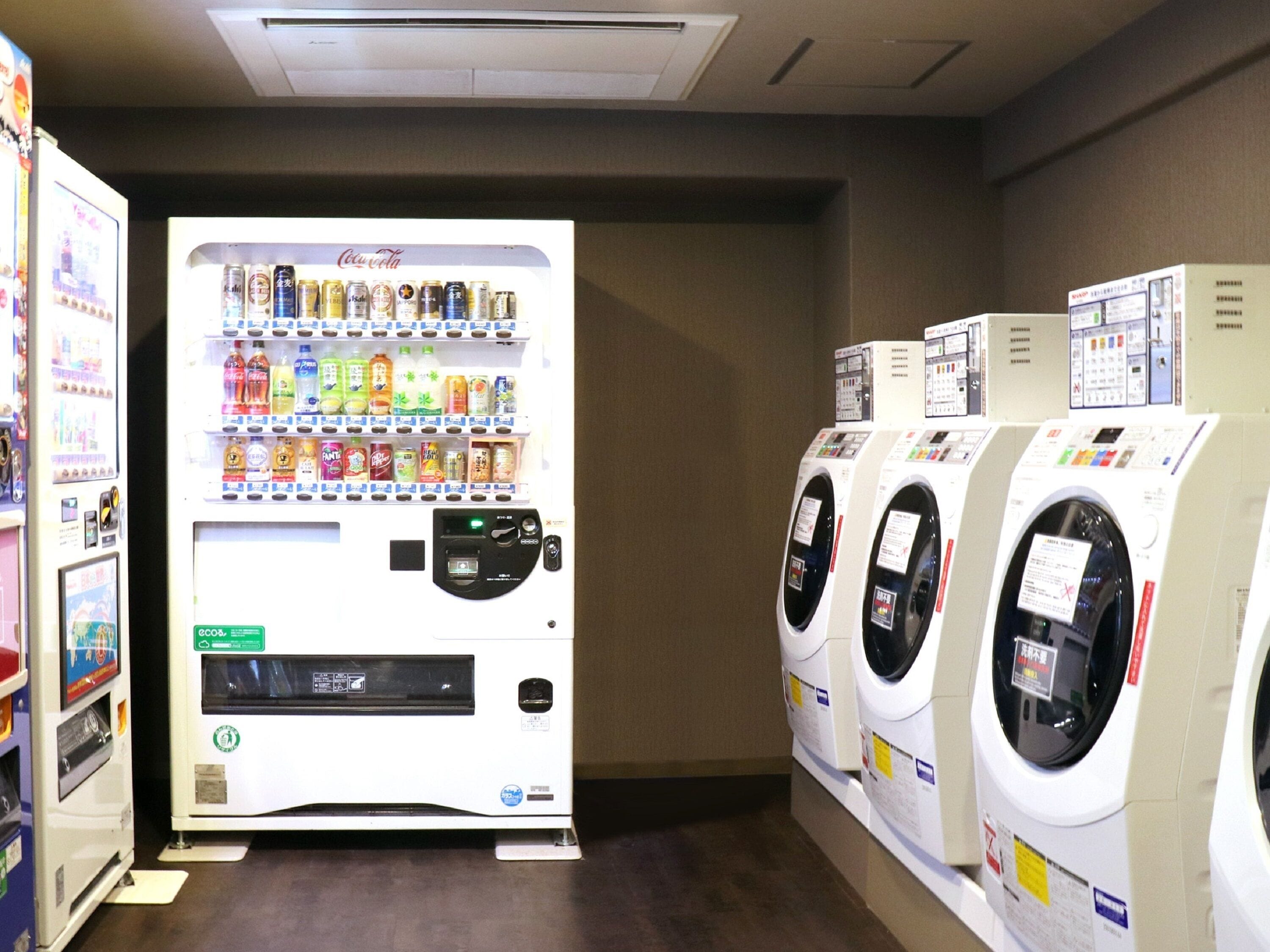 A laundromat with a vending machine selling beverages and a row of washing machines.