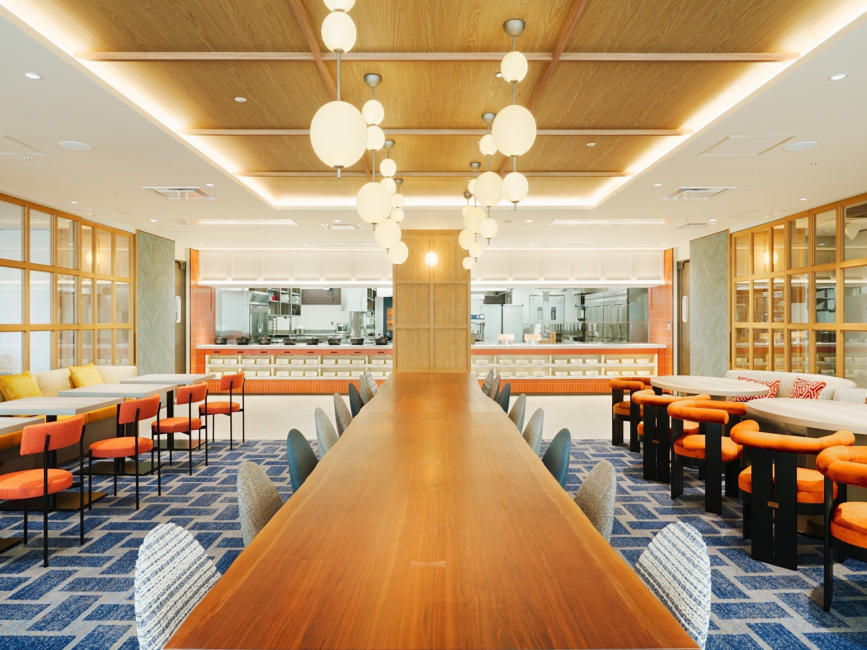 Un comedor amplio con una larga mesa de madera, sillas anaranjadas y un diseño de techo moderno con lámparas esféricas colgantes.