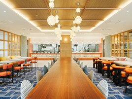 A spacious dining area with a long wooden table, orange chairs, and a modern ceiling design with hanging spherical lights.