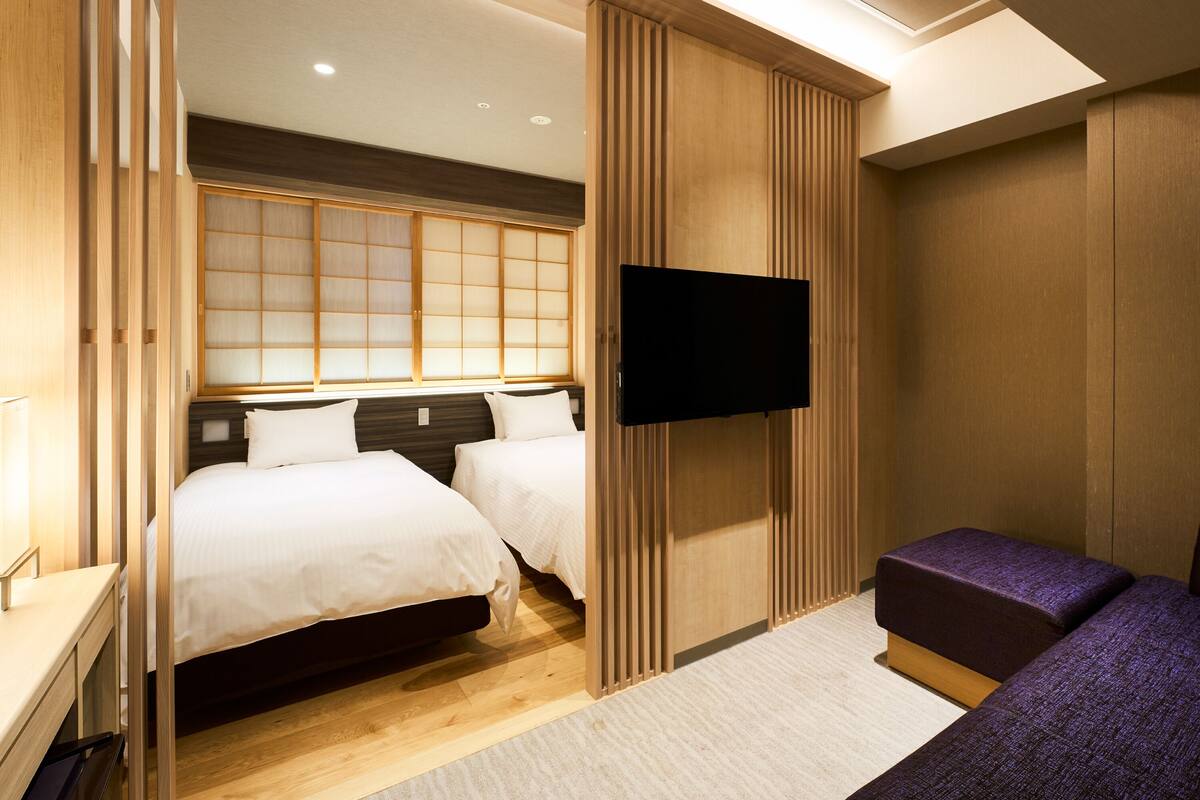 Ein Hotelzimmer mit zwei Betten, einem Fernseher und einer Schiebetür.