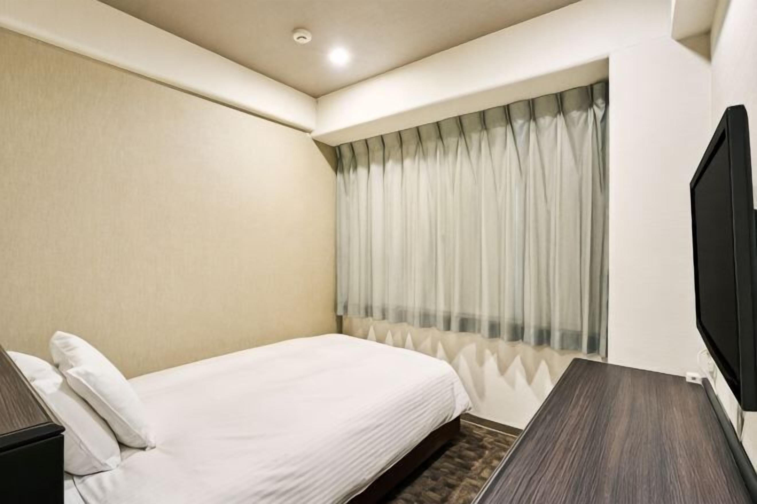Quarto de hotel com cama, televisão, janela com cortinas e televisão fixada na parede.