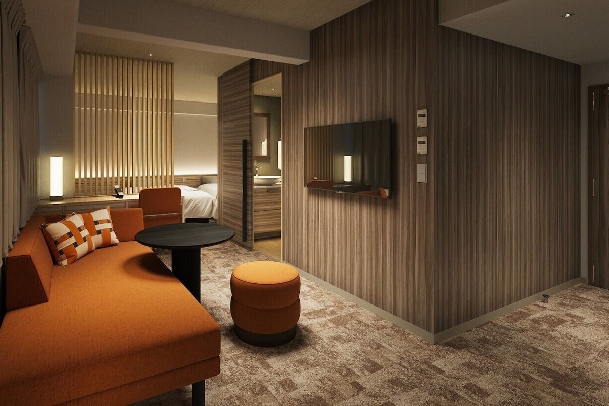 A modern hotel room with a sofa, ottoman, TV, and a large mirror.