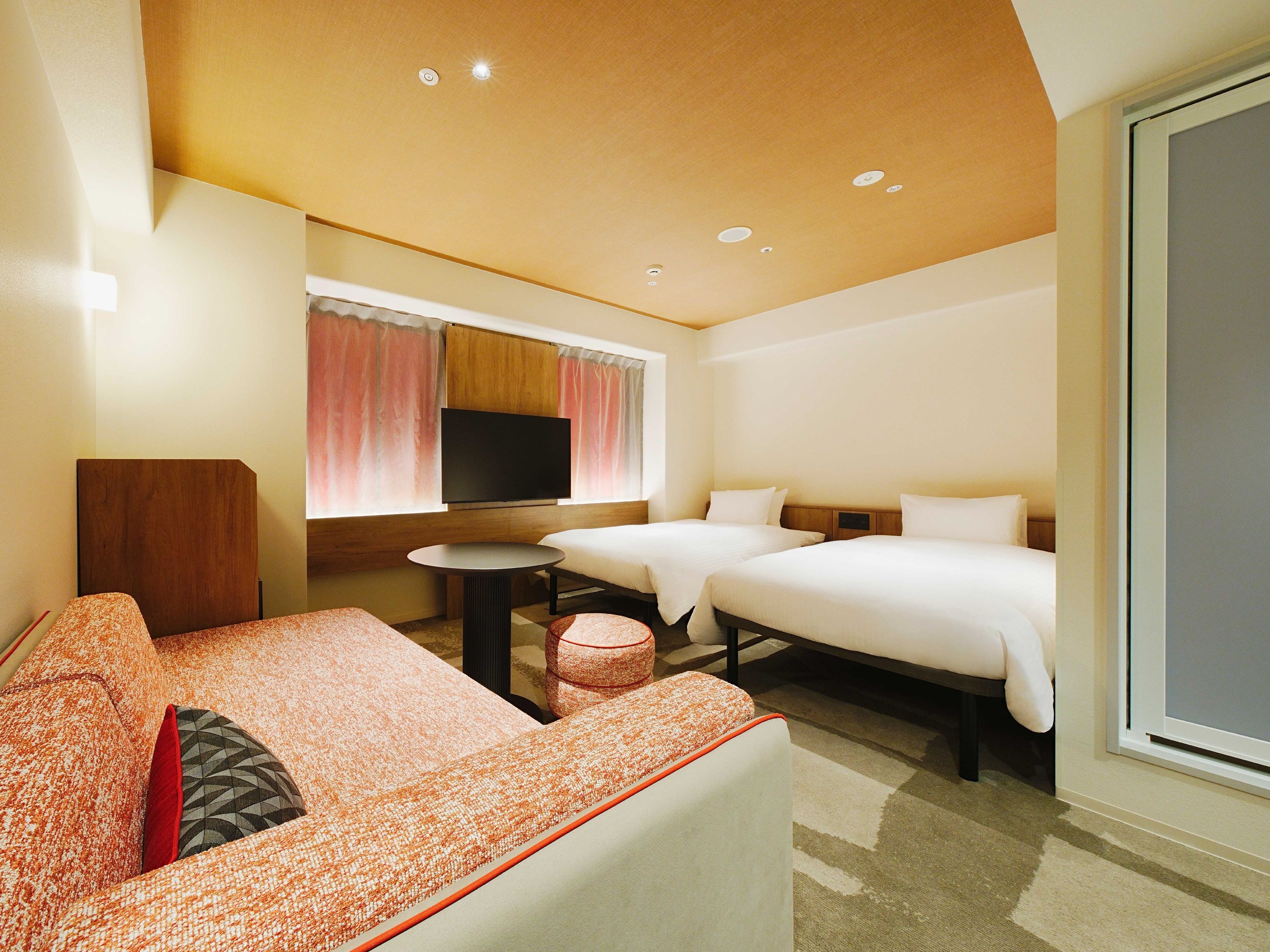 A hotel room with a sofa, two beds, a TV, and a small table.
