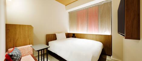 A hotel room with a bed, a small desk, a chair, and a window with curtains.