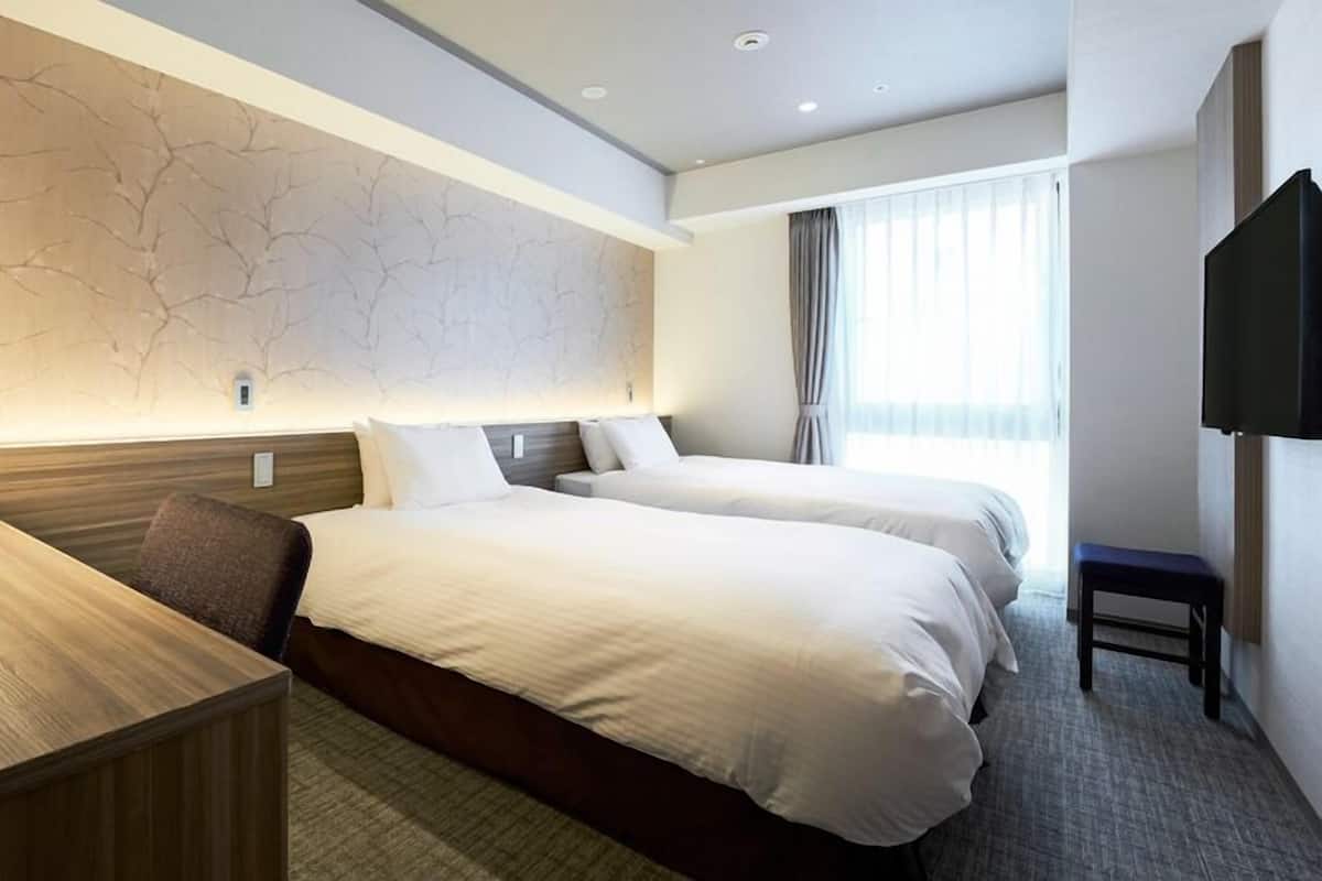 A hotel room with two beds, a desk, a chair, a TV, and a window with curtains.