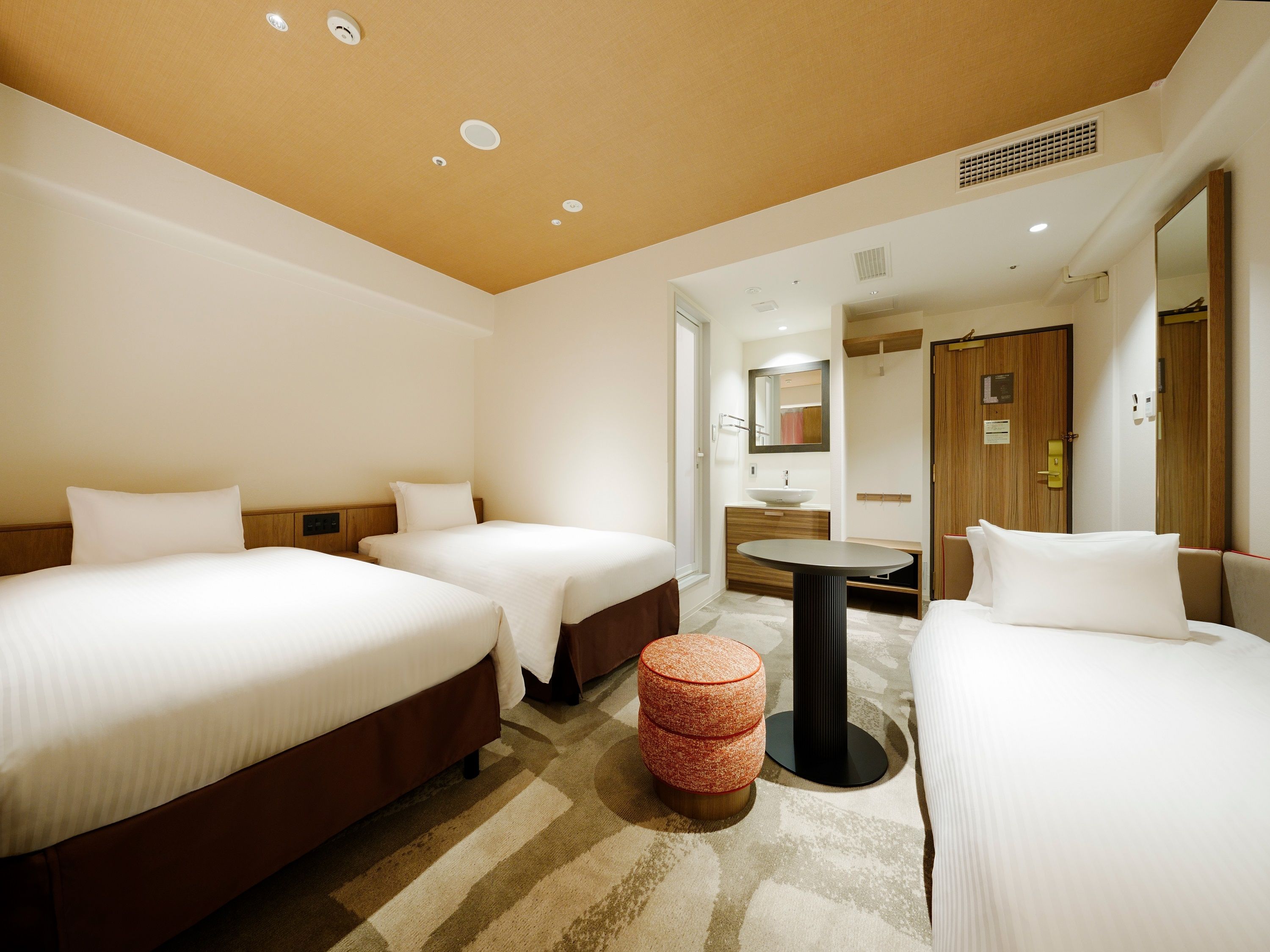 Habitación de hotel con dos camas, una mesa redonda pequeña, un espejo y una puerta de madera.