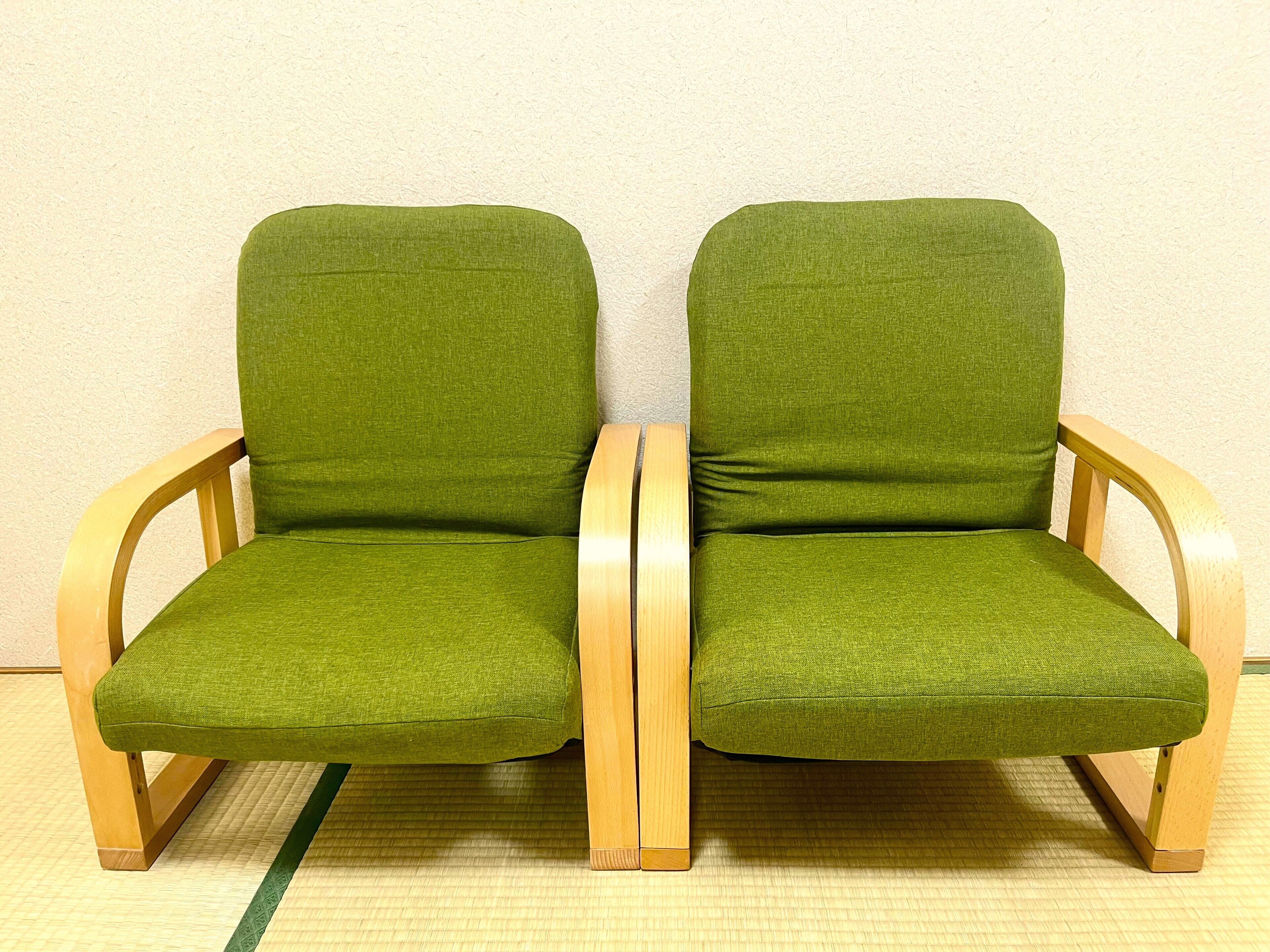 Due poltrone verdi imbottite con gambe in legno e un tappetino coordinato verde.