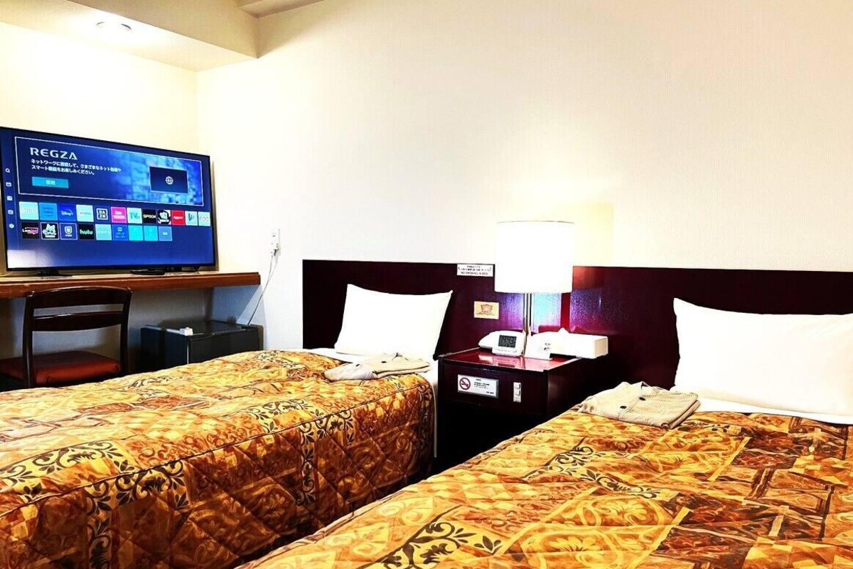 A hotel room with two beds, a television, a desk, and a nightstand with a lamp.