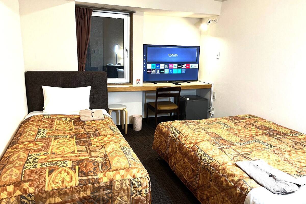 A hotel room with two beds, a desk with a computer, a chair, and a small table.