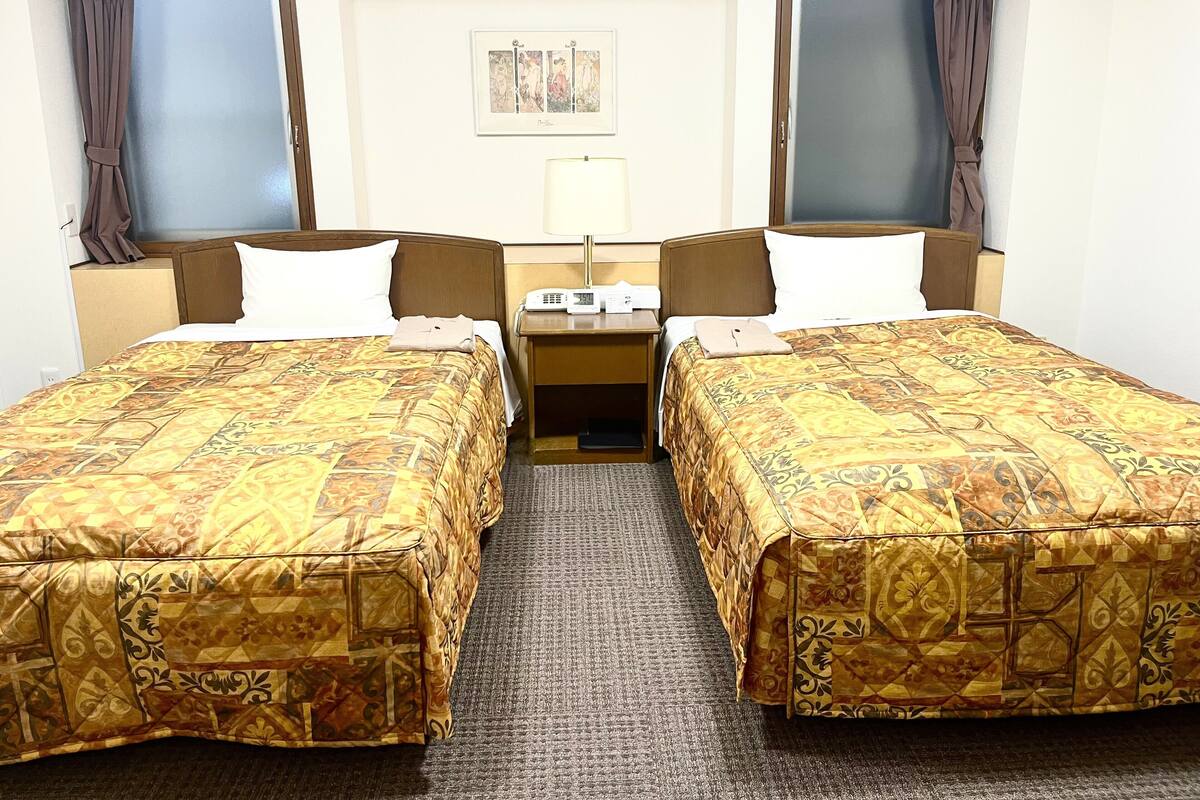 A hotel room with two single beds, a desk, and a chair.