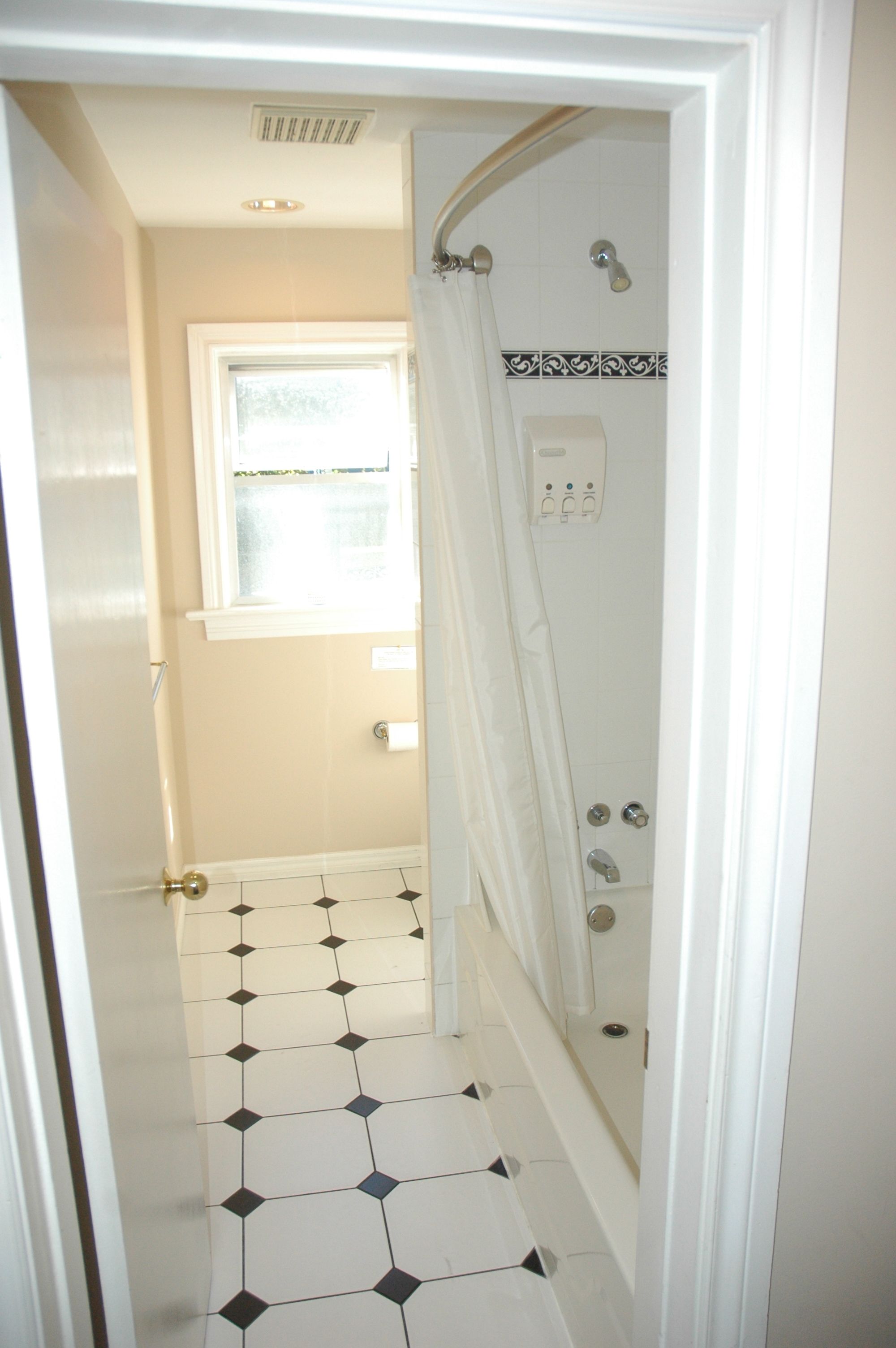 Un pasillo estrecho con suelo de baldosas que conduce a un baño con ducha y ventana.