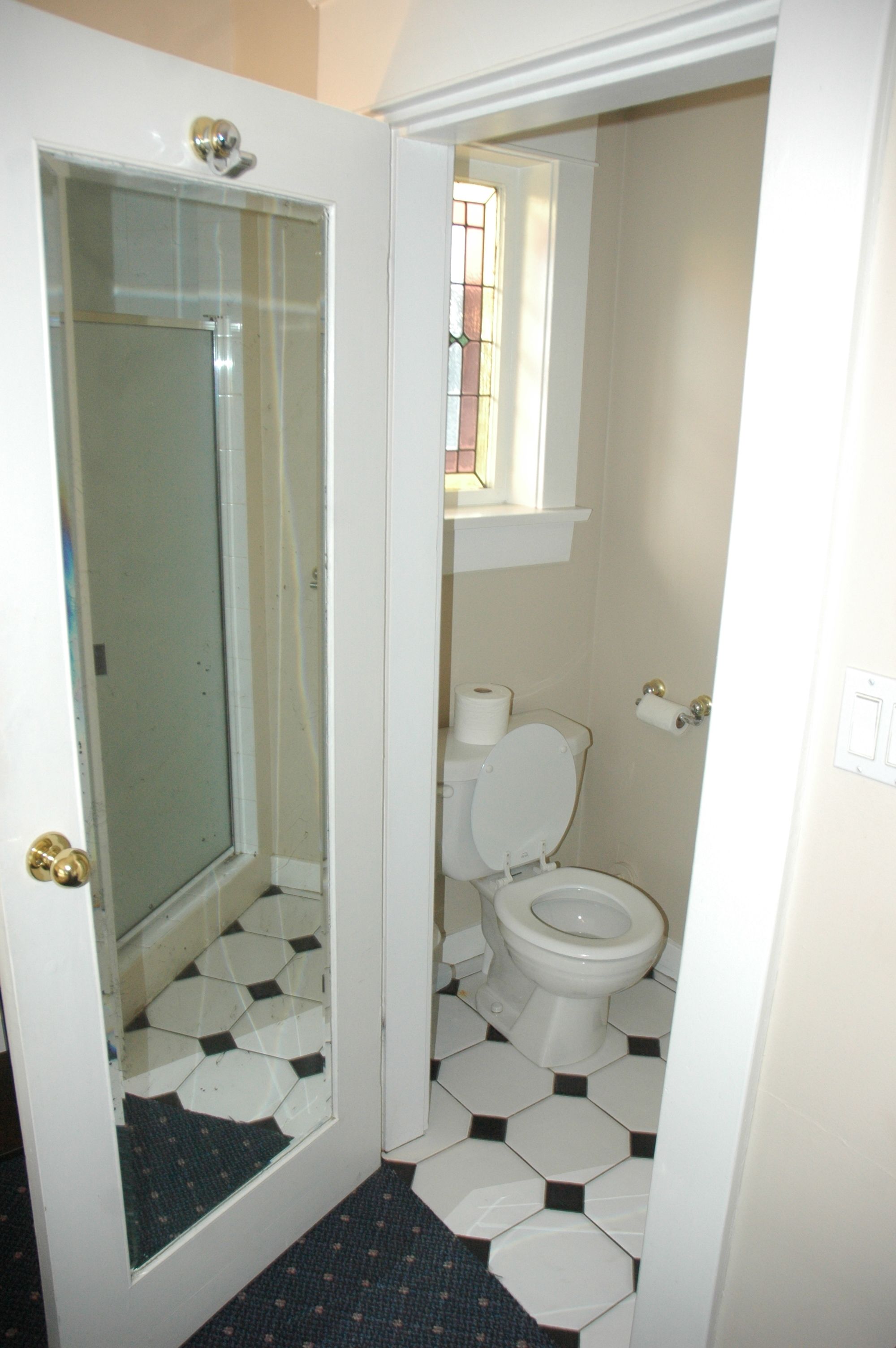A bathroom with a toilet, a glass shower enclosure, and a small window.