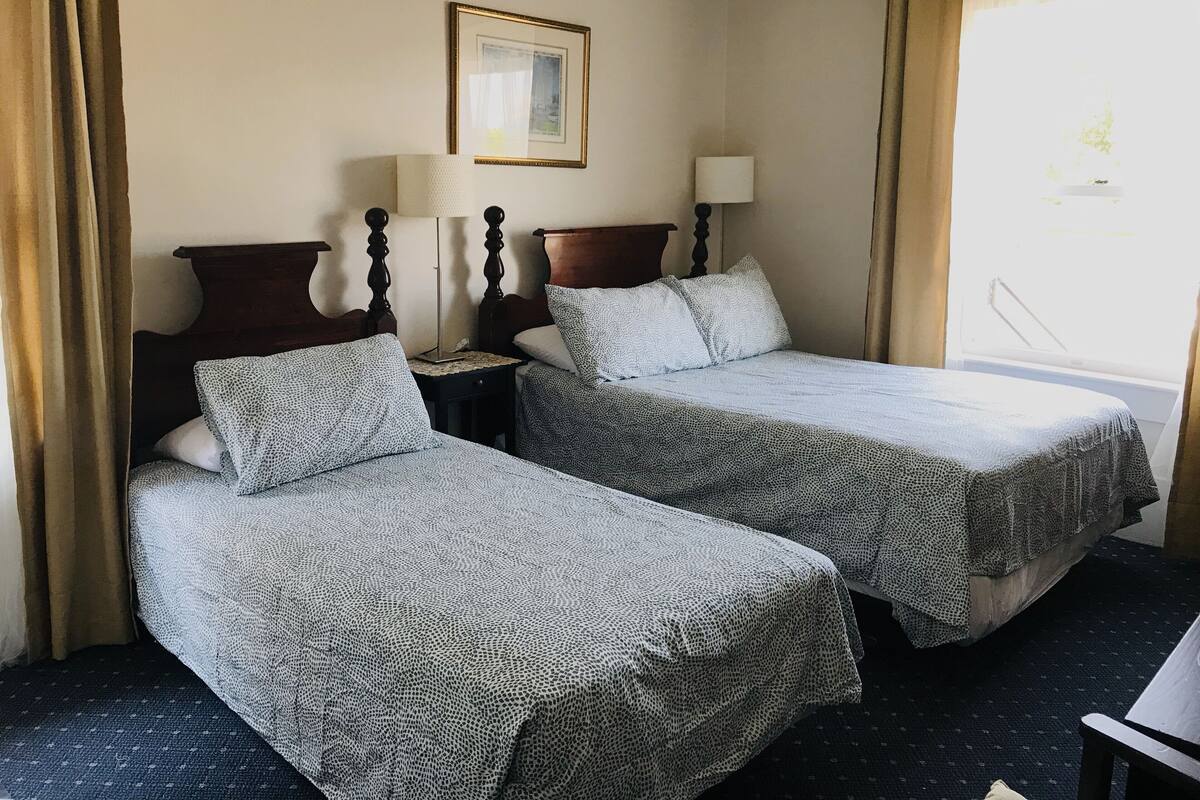 A hotel room with two beds, a framed picture on the wall, and a window with curtains.