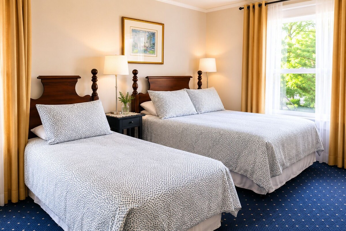 A hotel room with two beds, a nightstand, lamps, a framed picture on the wall, and a window with curtains.