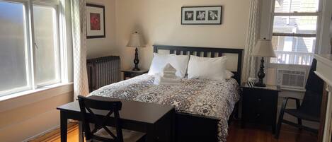 A neatly arranged bedroom with a bed, bedside table, lamp, chair, and a window with curtains.
