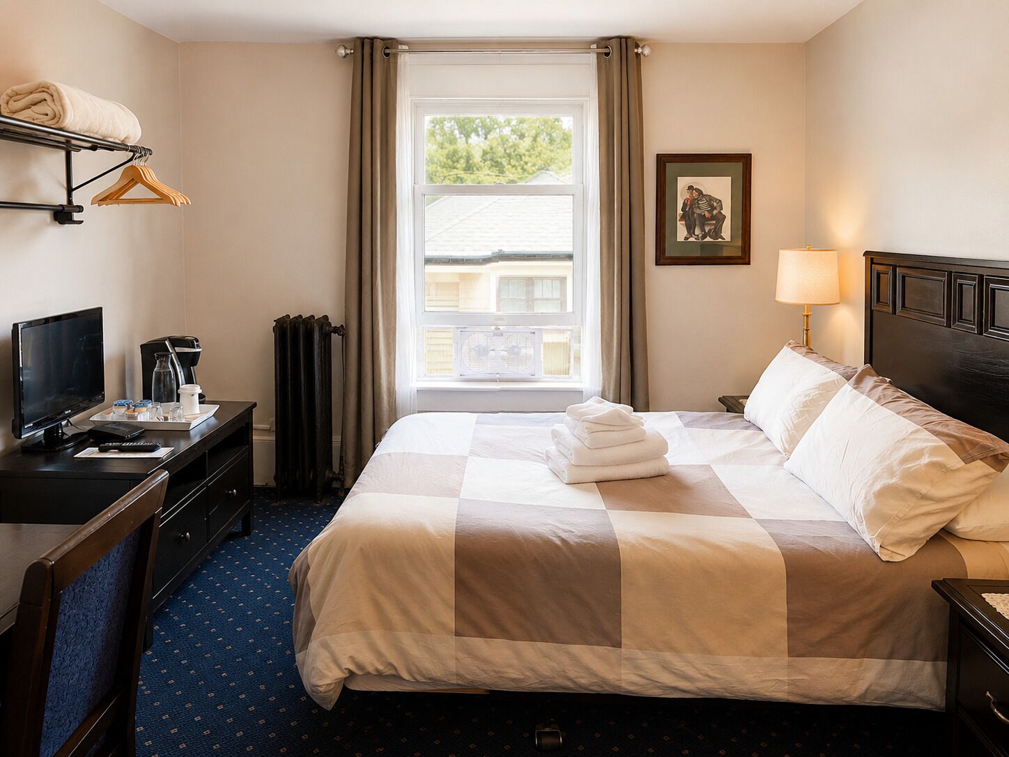 A hotel room with a bed, a desk with a computer, a TV, and a window with curtains.