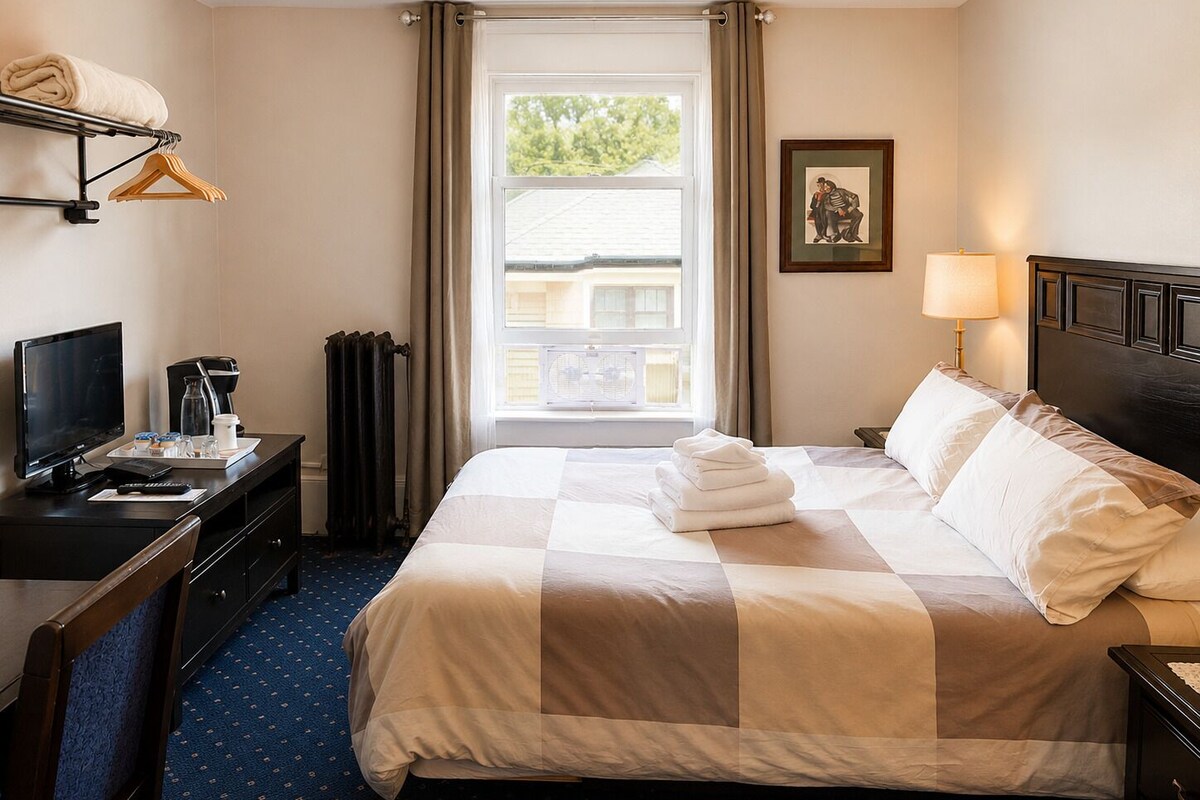A hotel room with a bed, a desk with a computer, a TV, and a window with curtains.