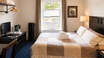 A hotel room with a bed, a desk with a computer, a TV, and a window with curtains.