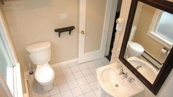 Une salle de bain avec des toilettes, un lavabo et un miroir. Il y a un porte-serviettes au-dessus des toilettes et une étagère au-dessus du lavabo.