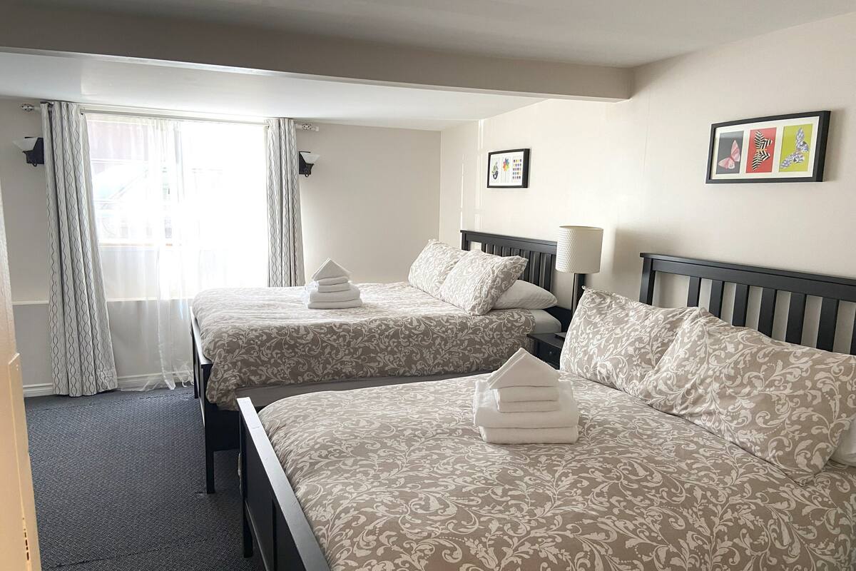 A hotel room with two beds, a nightstand, a lamp, and a window with curtains.