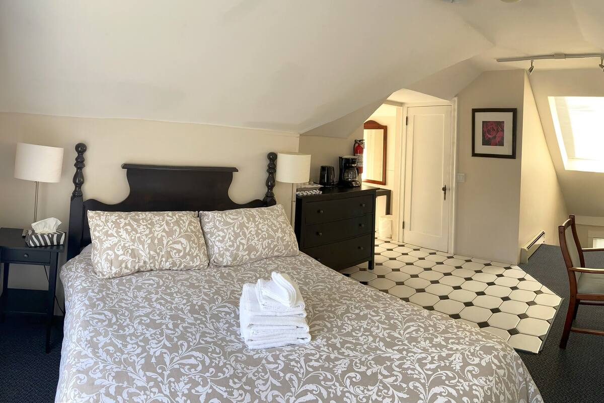 A hotel room with a bed, a desk, a chair, a microwave, and a door leading to another room.