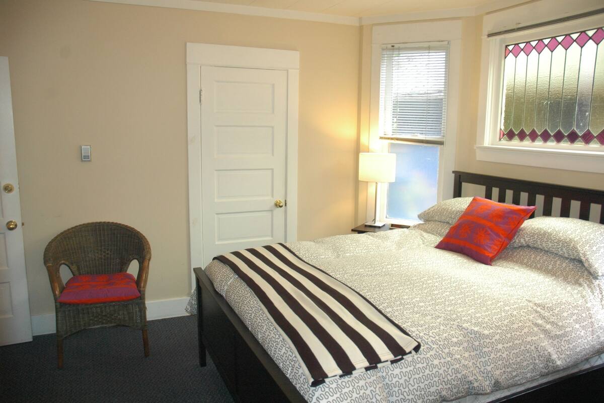 A bedroom with a bed, a chair, a door, and a window with blinds.