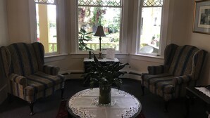 A room with two patterned armchairs, a round table with a lace tablecloth, and a potted plant. - Douglas Guest House (Vancouver)