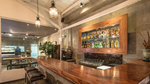 A bar area with a wooden counter, stools, and a shelf of liquor bottles. - Kejora Suites (Denpasar)