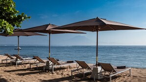 Ein Strand mit Liegestühlen und Sonnenschirmen, ein Boot im Wasser und ein Berg im Hintergrund.