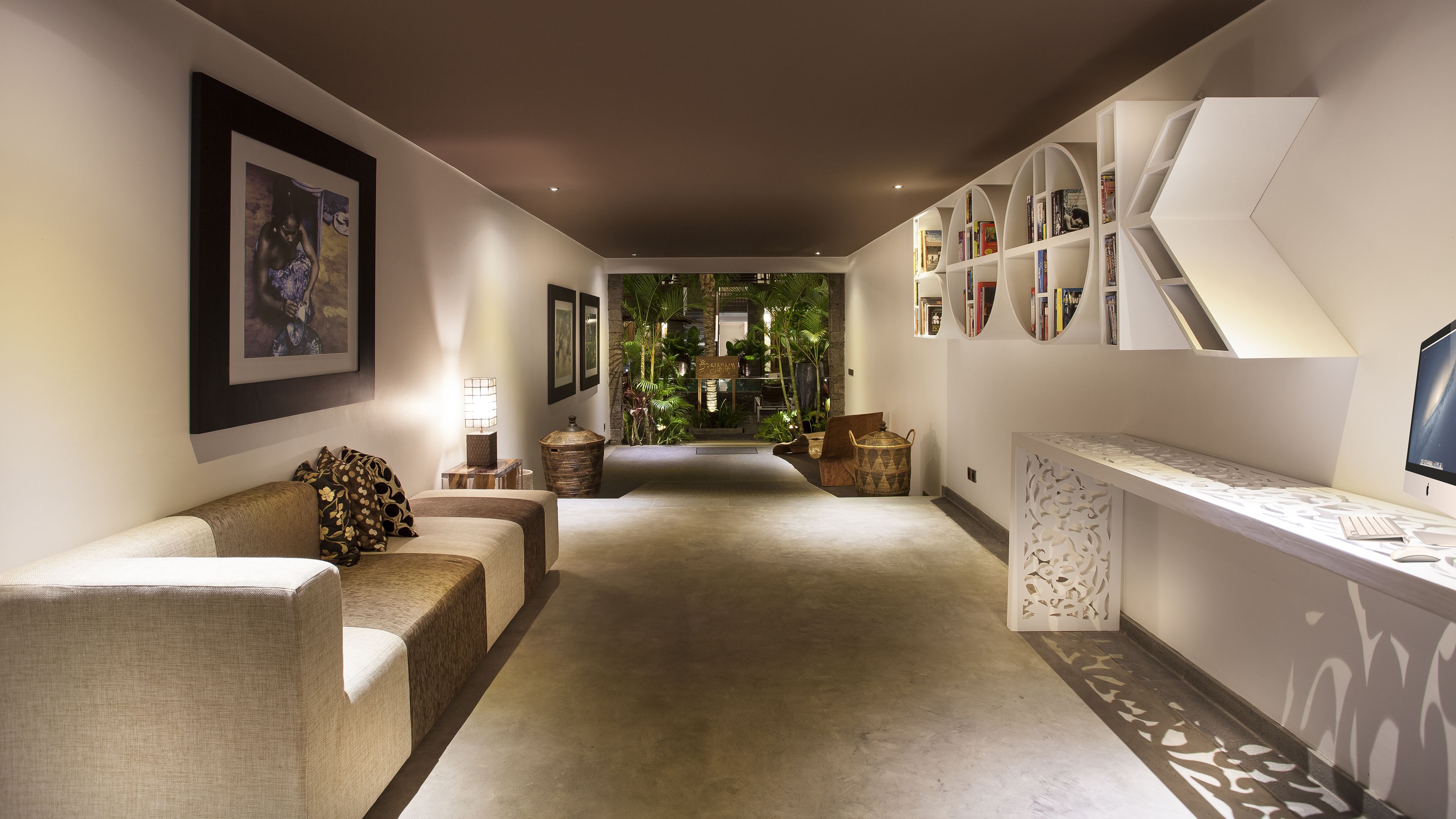A modern interior with a sofa, a desk with a computer, and a bookshelf.