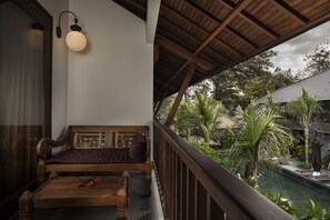 Un banc en bois avec des coussins, une petite table agrémentée de fleurs et une vue sur une piscine et la verdure environnante.