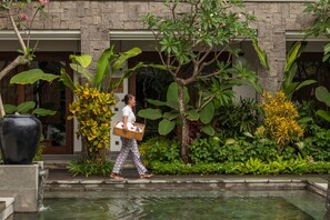 Une personne qui passe devant un bâtiment agrémenté d’un élément d’eau et d’une végétation luxuriante.