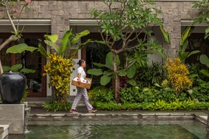 A person walking past a building with a water feature and lush greenery.