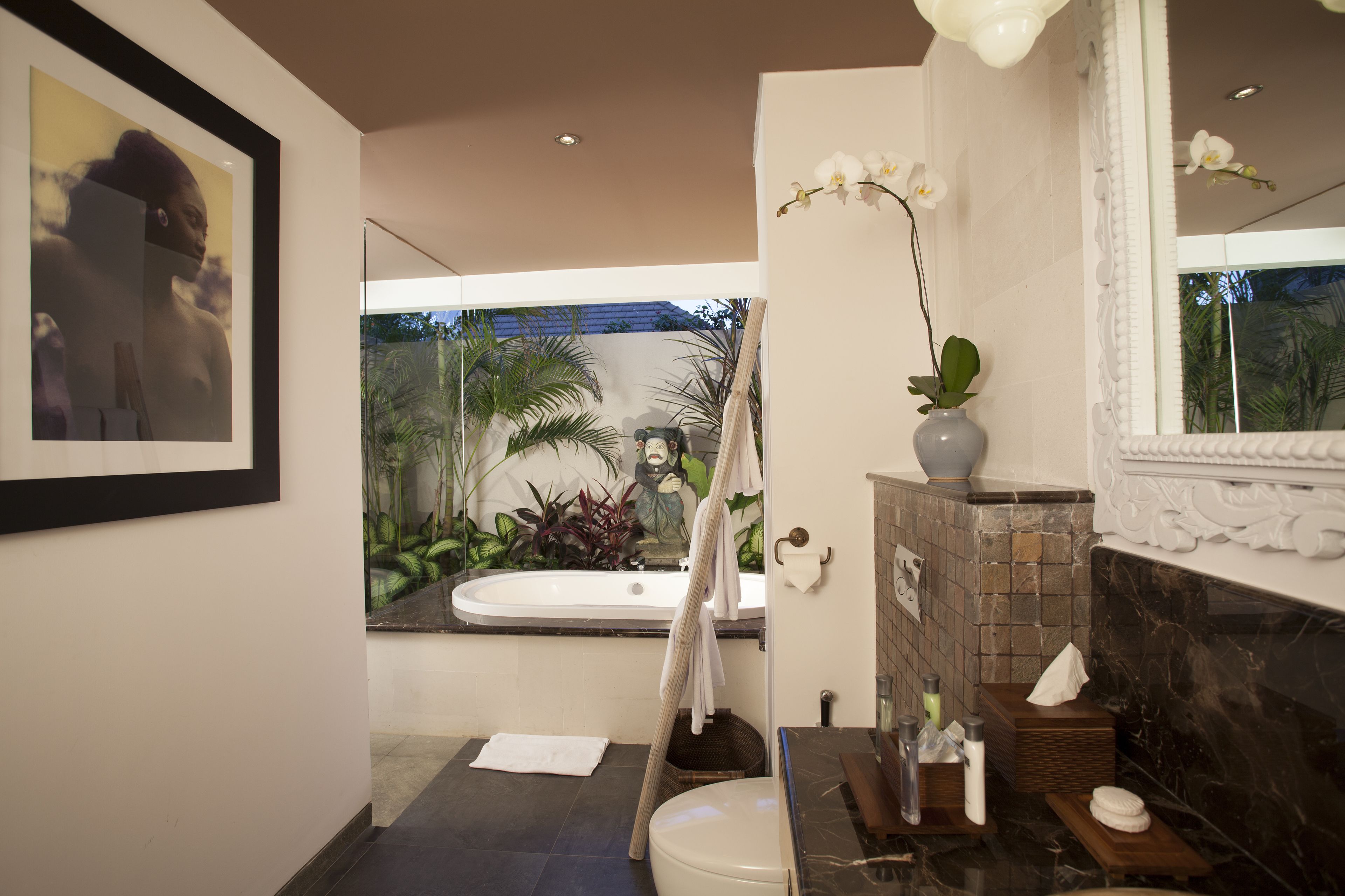 Ein modernes Badezimmer mit einer Badewanne, Toilette und Waschbecken. Es gibt einen Spiegel, einen Handtuchhalter und eine Vase mit einer Orchidee.