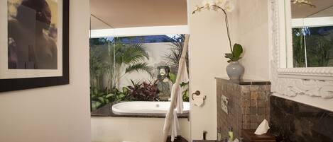 Ein modernes Badezimmer mit einer Badewanne, Toilette und Waschbecken. Es gibt einen Spiegel, einen Handtuchhalter und eine Vase mit einer Orchidee.