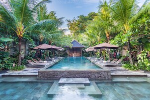A pool with lounge chairs and umbrellas, surrounded by lush greenery.