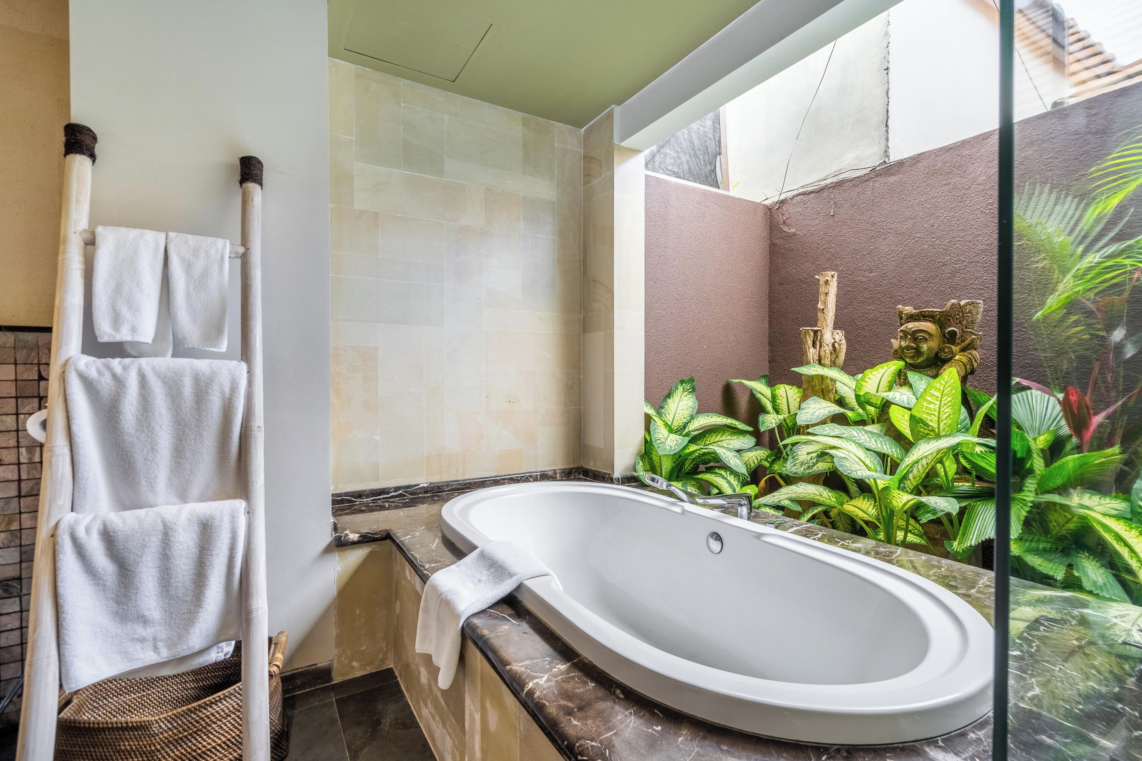 A bathroom with a large oval sink, a towel rack with two towels, a wooden ladder, and a decorative statue.