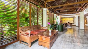A spacious lobby with a wooden bench, a small table with a vase, and a decorative wall. - Kejora Suites (Denpasar)