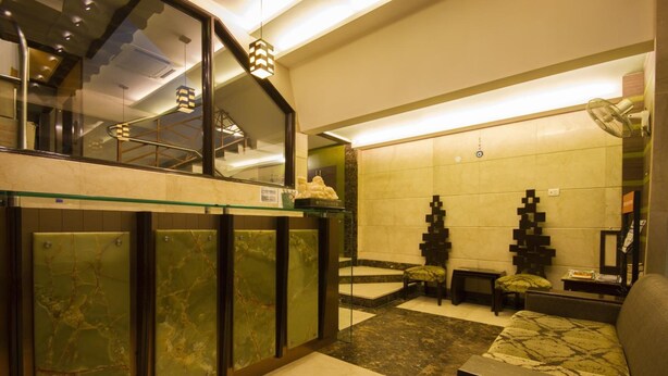 Un moderno vestíbulo de hotel con barandilla de vidrio, una zona de estar con cojines estampados y una pared decorativa con formas geométricas.