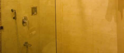 A glass-enclosed shower with a handheld showerhead, a wall-mounted faucet, and a towel rack with folded towels.